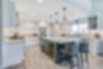 Modern kitchen with white cabinets, marble countertops, and gray bar stools. Stainless steel appliances and pendant lights create a sleek look.