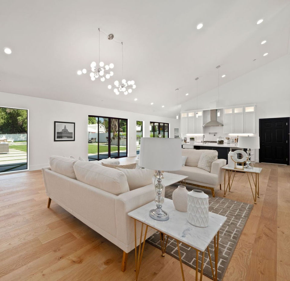 Spacious modern living room with white sofas, chandelier, and open kitchen with bar stools in the background.