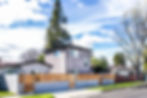 Modern gray two-story house with wooden fence in sunny suburban neighborhood. Tall tree behind, blue sky with clouds. Peaceful mood.