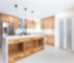 Modern kitchen with wooden cabinets, white countertops, stainless steel fridge, red pendant lights, and a central island with black faucet.