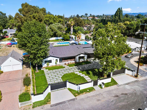 Aerial view of a modern house with a geometric patio, large trees, and a pool in a suburban neighborhood.