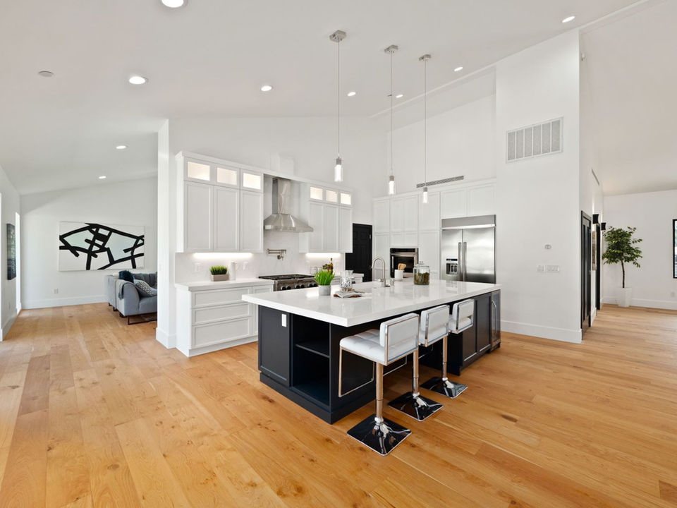 Modern kitchen with a large island, pendant lights, and sleek appliances. Open living space with hardwood floors.