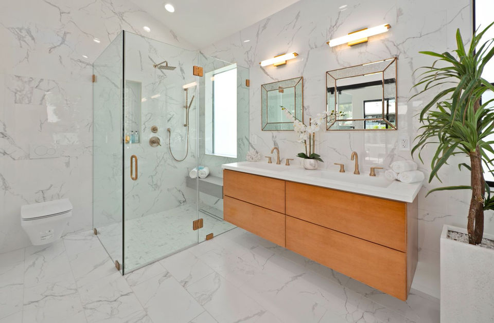 Modern white bathroom with glass shower, wooden vanity, mirrors, and decorative plants.