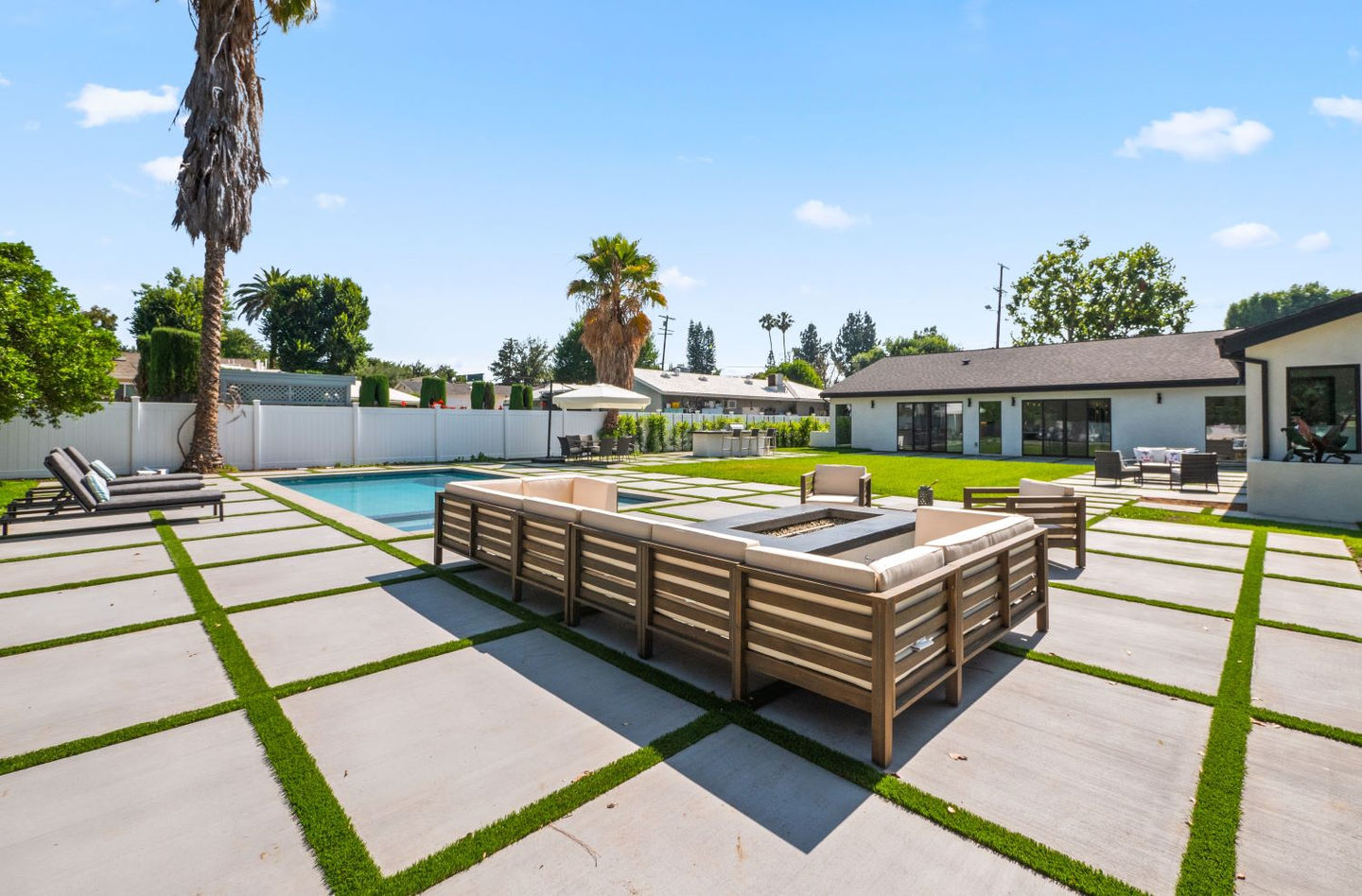 Modern backyard with a pool, patio furniture, and palm trees on a sunny day.