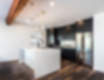 Modern kitchen with dark cabinets, stainless steel fridge, and white island. Wooden beam ceiling and hardwood floor. Bright and sleek.
