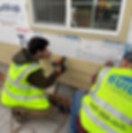 Two construction workers in safety vests expertly plan the installation of siding, bringing the design-build process vision to life on a building wall.
