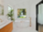 Modern bathroom with a large white bathtub, gold fixtures, a wooden vanity, and a green plant by the window, brought to life through expert planning.