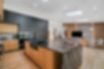 Modern kitchen and living room with black and wood cabinets, marble island, sleek design. Skylights and wood accents create a bright, cozy feel.