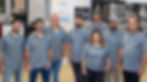 A group of eight people in matching gray Built to Perfection shirts stands smiling in an office, representing superior craftsmanship.