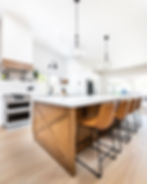 Modern kitchen with a large wooden island, four brown stools, and pendant lights in a white interior design, in Los Angeles.