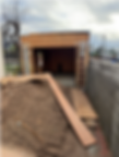 A wooden structure under construction with a ladder leaning against it. Dirt and wooden planks are scattered around. Cloudy sky above.
