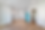 Bright, empty room with wood floors, white walls, and recessed lighting. Blue fridge in kitchen area; open door to small bathroom. Minimalist style.